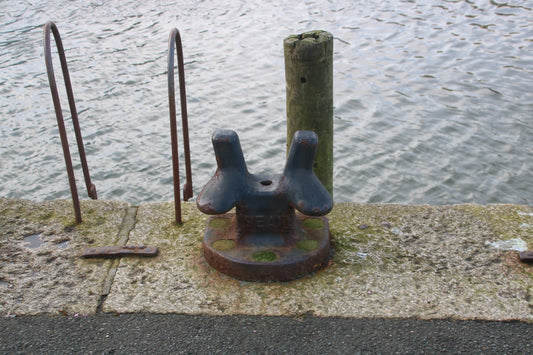 Rusty metal mooring bitt on concrete dock with wooden post and water background