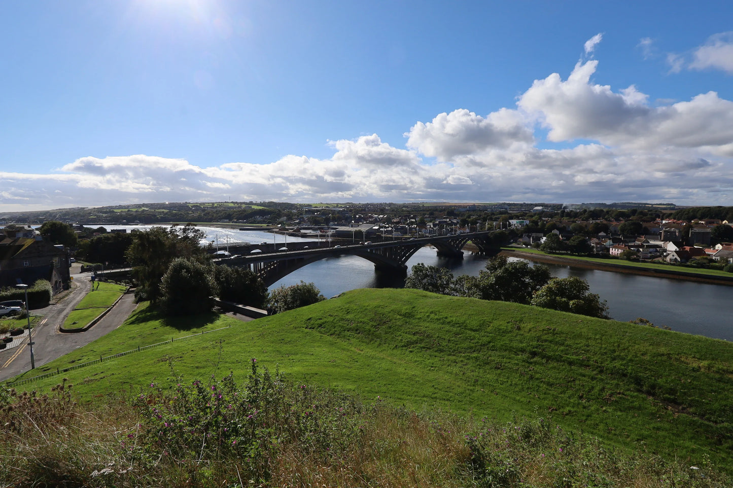 Scenic British landscape with arched bridge over river, green hills, and town under blue sky