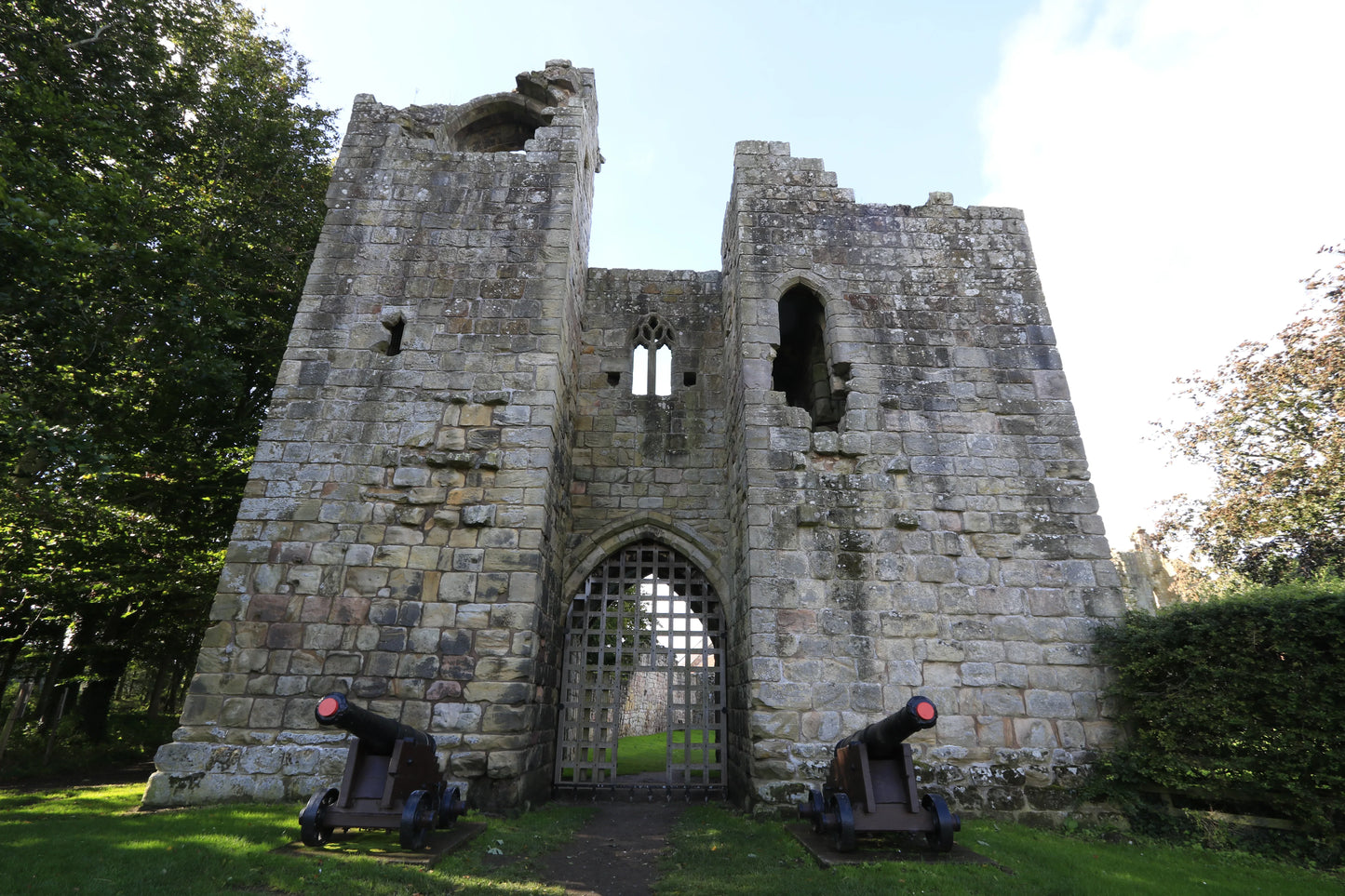 Historic stone castle gate with portcullis and two cannons on green lawn