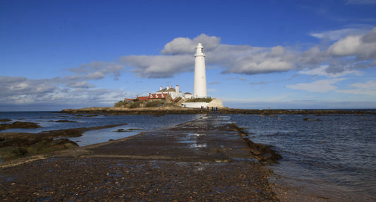 St Mary lighthouse on a rocky island connected by a causeway under blue sky, Northumberland coast landscape