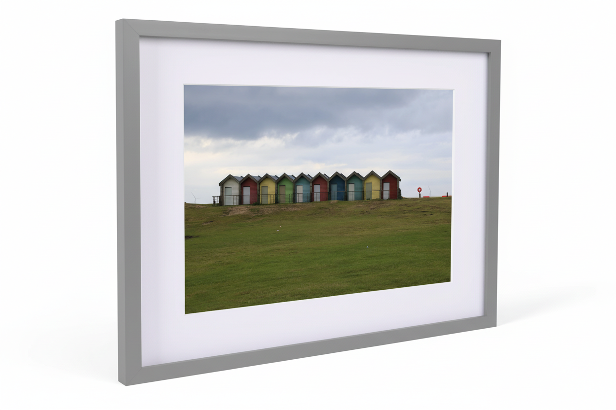 Framed print of Blyth beach huts in varied colors on grassy hill under cloudy sky