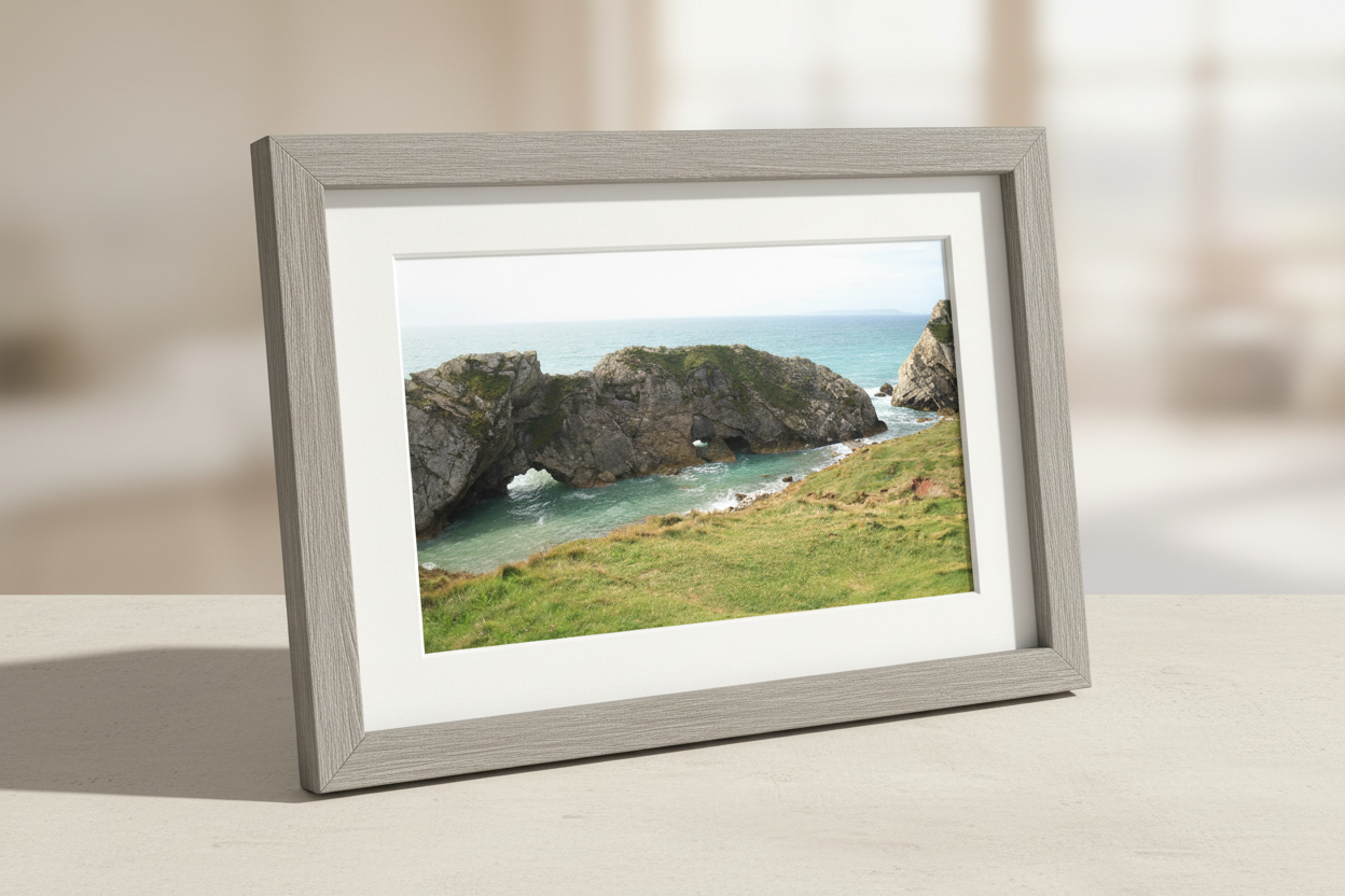 Framed print of Dorset coastline with rocky arch formation, green cliffs, and turquoise sea waves