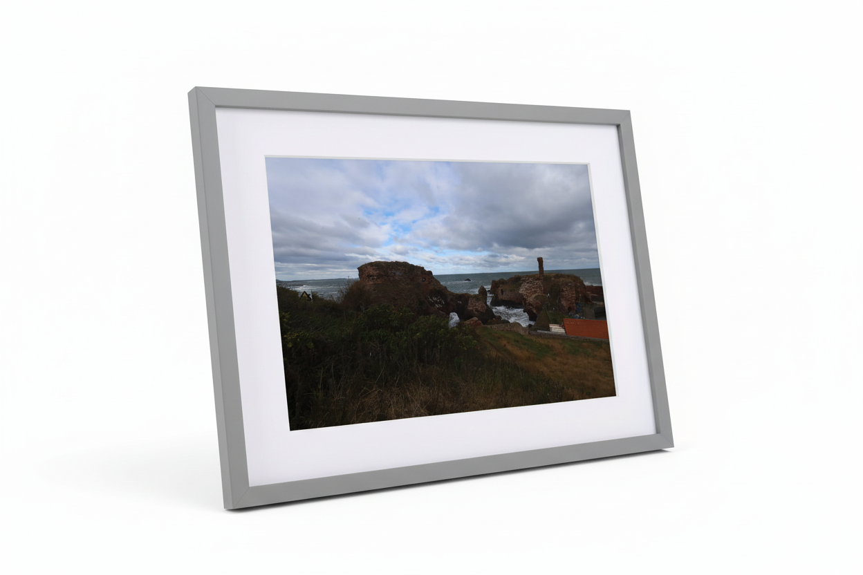 Framed print of Dunbar coastal ruins with rocky cliffs, grassy foreground, and cloudy sky