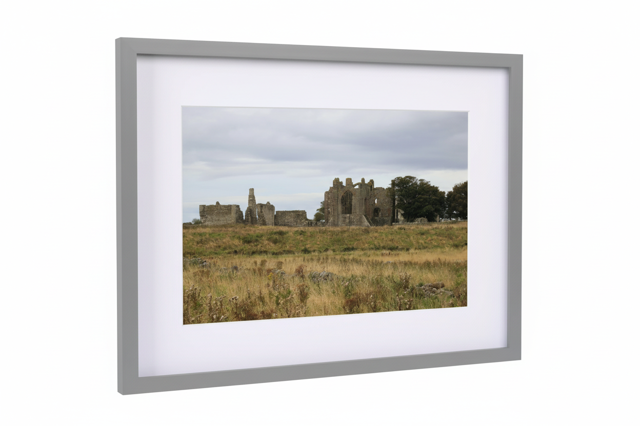 Framed photo of Lindisfarne Priory ruins in grassy field under cloudy sky, British landscape scene