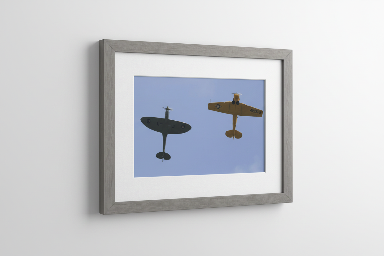 Framed print of Spitfire and yellow aircraft flying overhead against blue sky, British aviation photo art