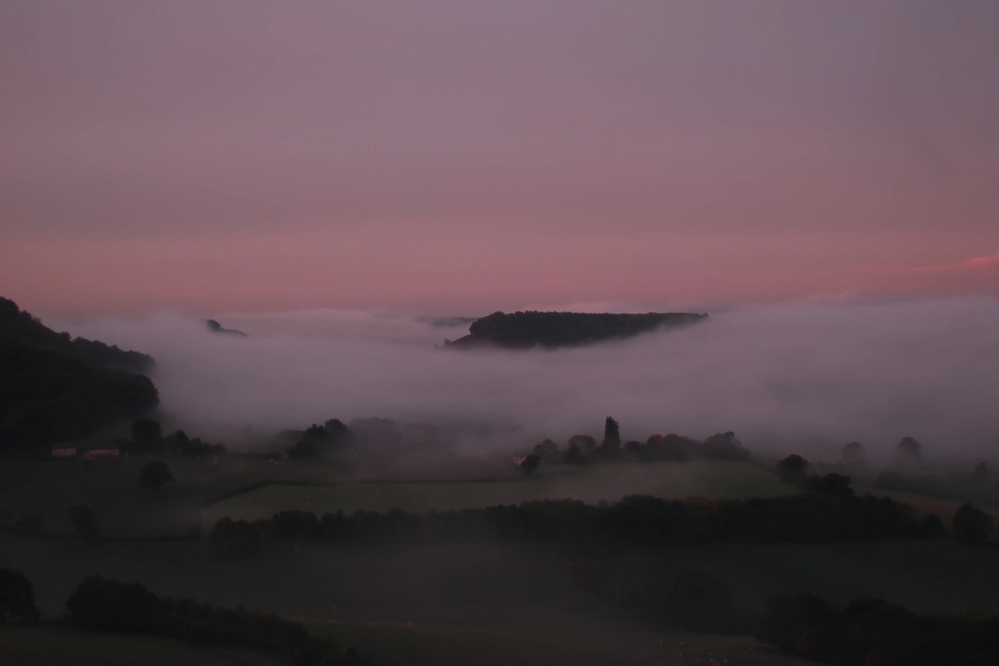 British landscape at dusk with rolling hills and low fog under pink and purple sky