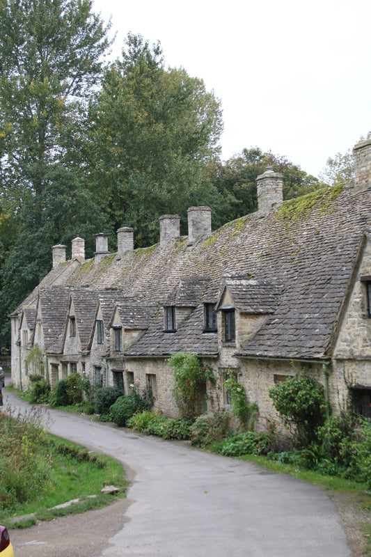 Row of historic British stone cottages with mossy roofs and garden greenery along a country lane