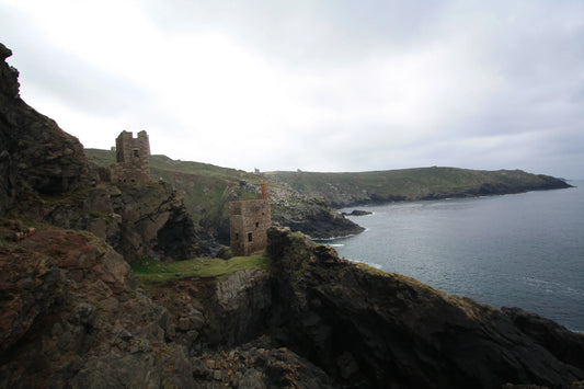 Historic stone mining engine houses on rocky cliffs overlooking calm sea at Cornwall coast under cloudy sky