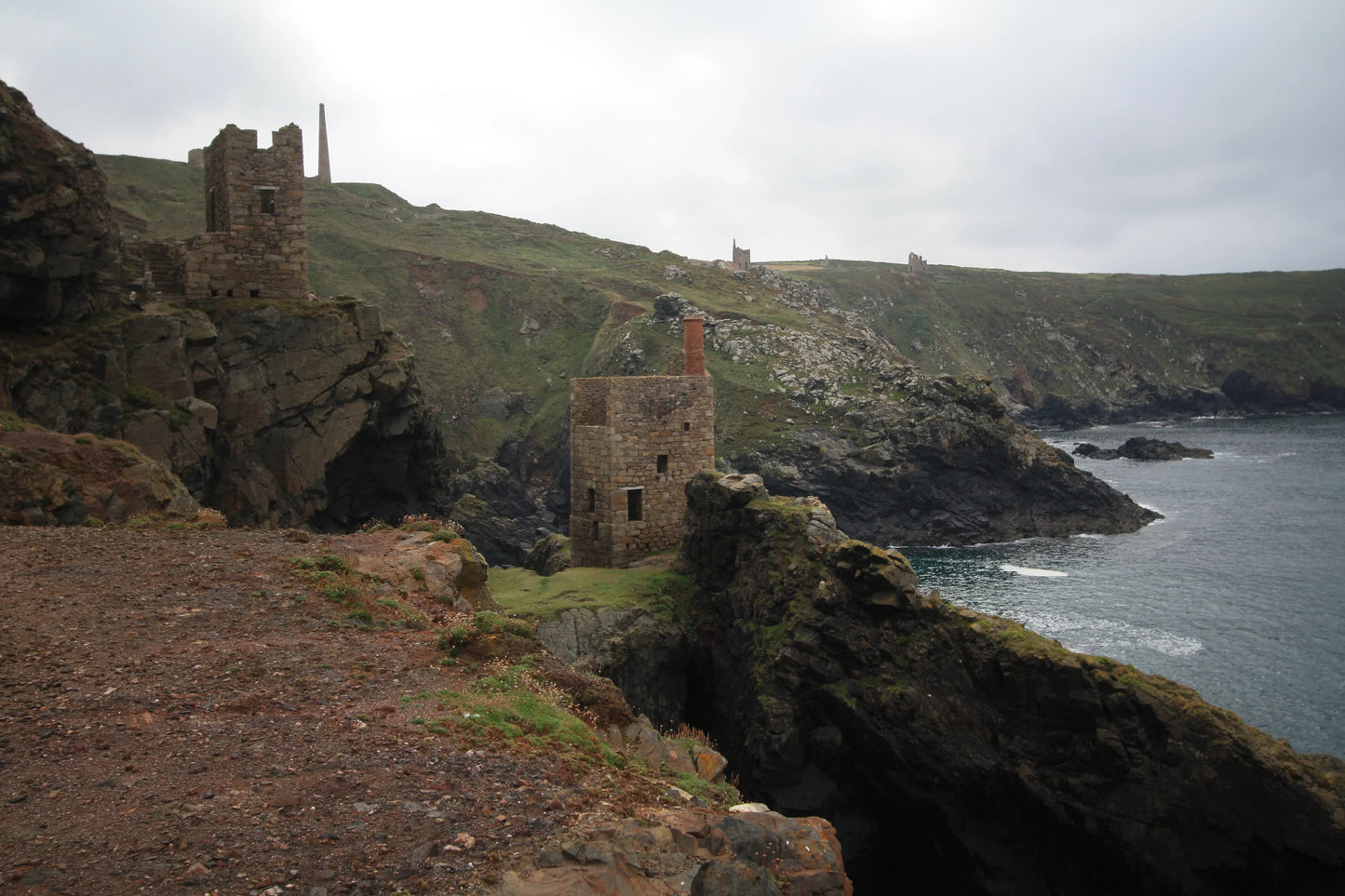 Ruined stone buildings on rugged cliffs overlooking sea at a British coastal landscape under cloudy sky
