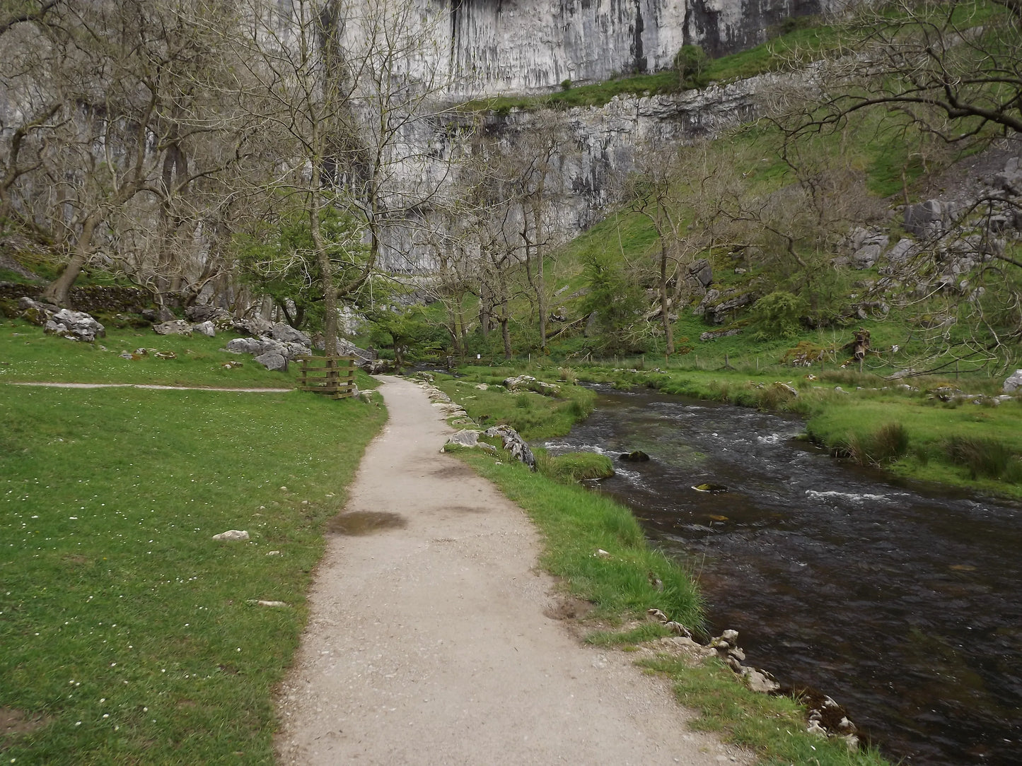 Walkway next to a flowing river with leafless trees and limestone cliffs in British countryside