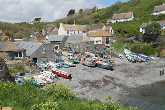 Small fishing village with stone cottages, colorful boats on pebble beach, and green hillside