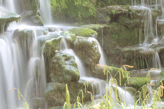 Moss-covered rocks with soft flowing water cascading over them in a serene natural waterfall