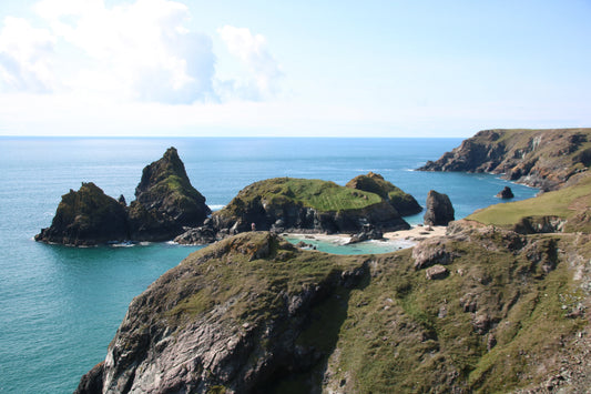 Rocky coastal cliffs and green hills overlooking blue sea and small sandy beach