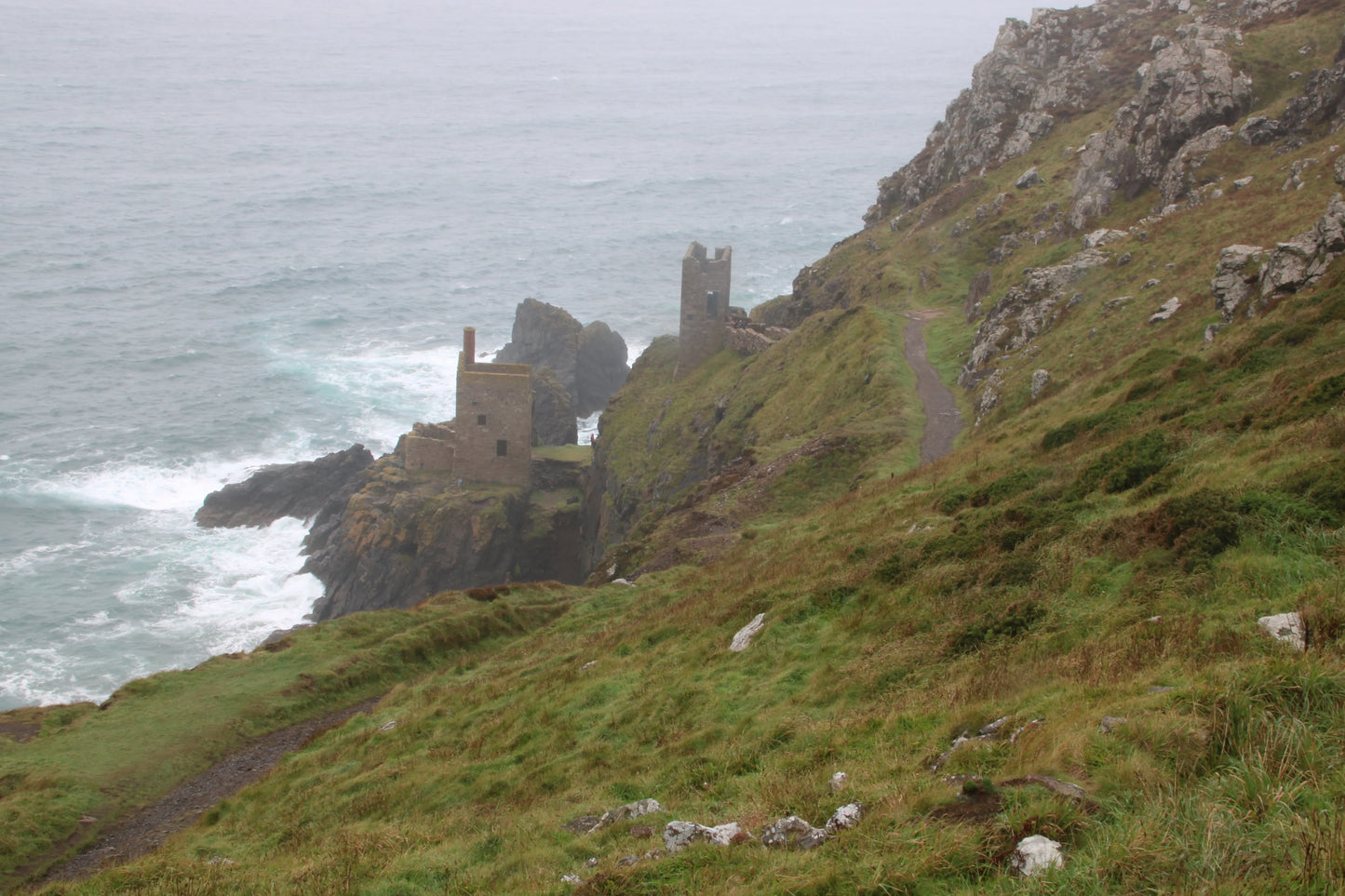 Stormy coastal scene at Botallack with historic Three Crowns engine house ruins on rugged cliffs and green hillside path