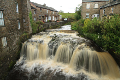 Waterfall flowing through a quaint British village with stone houses and lush greenery