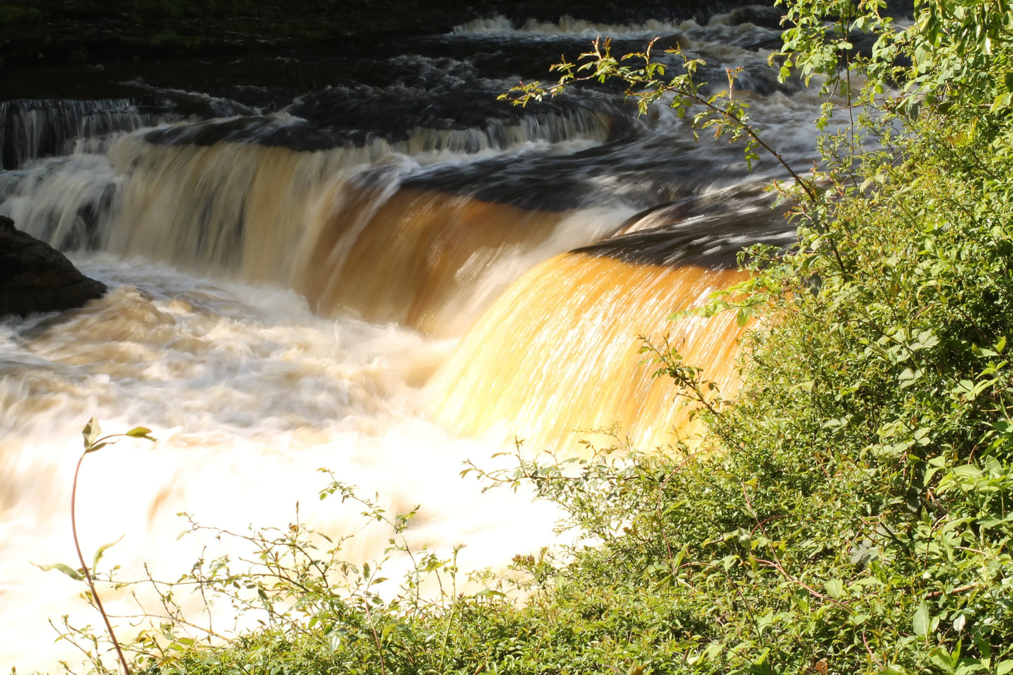British landscape featuring a sunlit waterfall cascading over rocks with lush green foliage