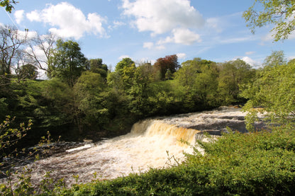 Scenic British waterfall surrounded by lush green trees and a partly cloudy blue sky