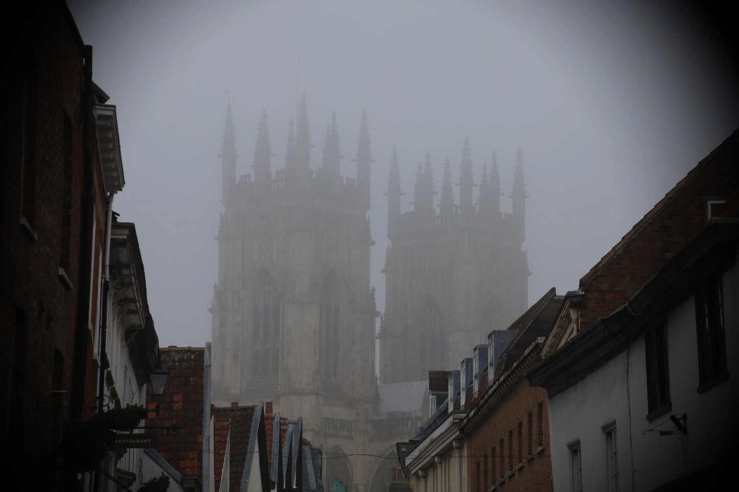 Foggy view of historic Gothic cathedral towers behind narrow street with traditional brick and tiled roofs