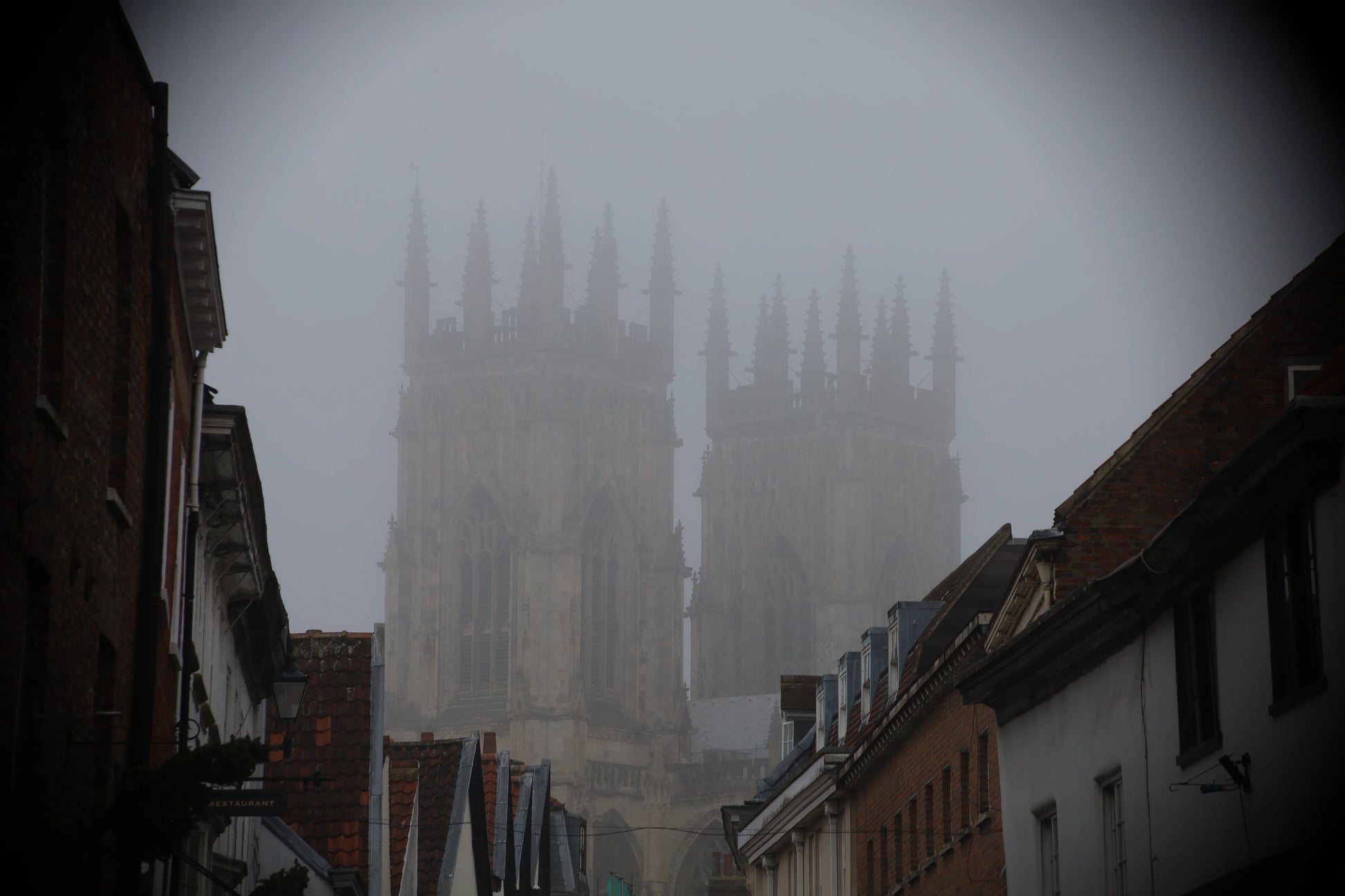 Foggy view of historic Gothic cathedral towers behind narrow street with traditional brick and tiled roofs
