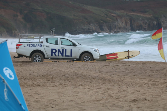 RNLI lifeguard truck parked on sandy beach next to rescue surfboard with ocean waves in background