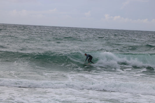 Surfer in a wetsuit riding a green wave at Praa Sands beach with cloudy sky