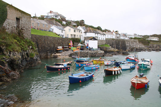 Colorful fishing boats moored in a small harbor with stone walls and coastal houses in the background