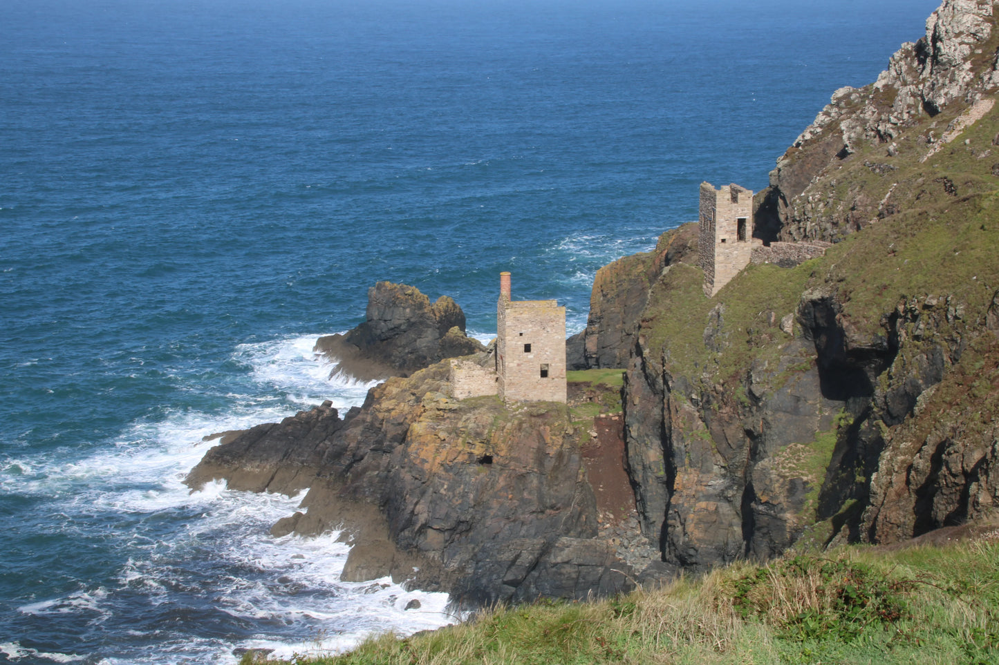 Ruined stone buildings on rocky cliffs by blue ocean waves in British coastal landscape