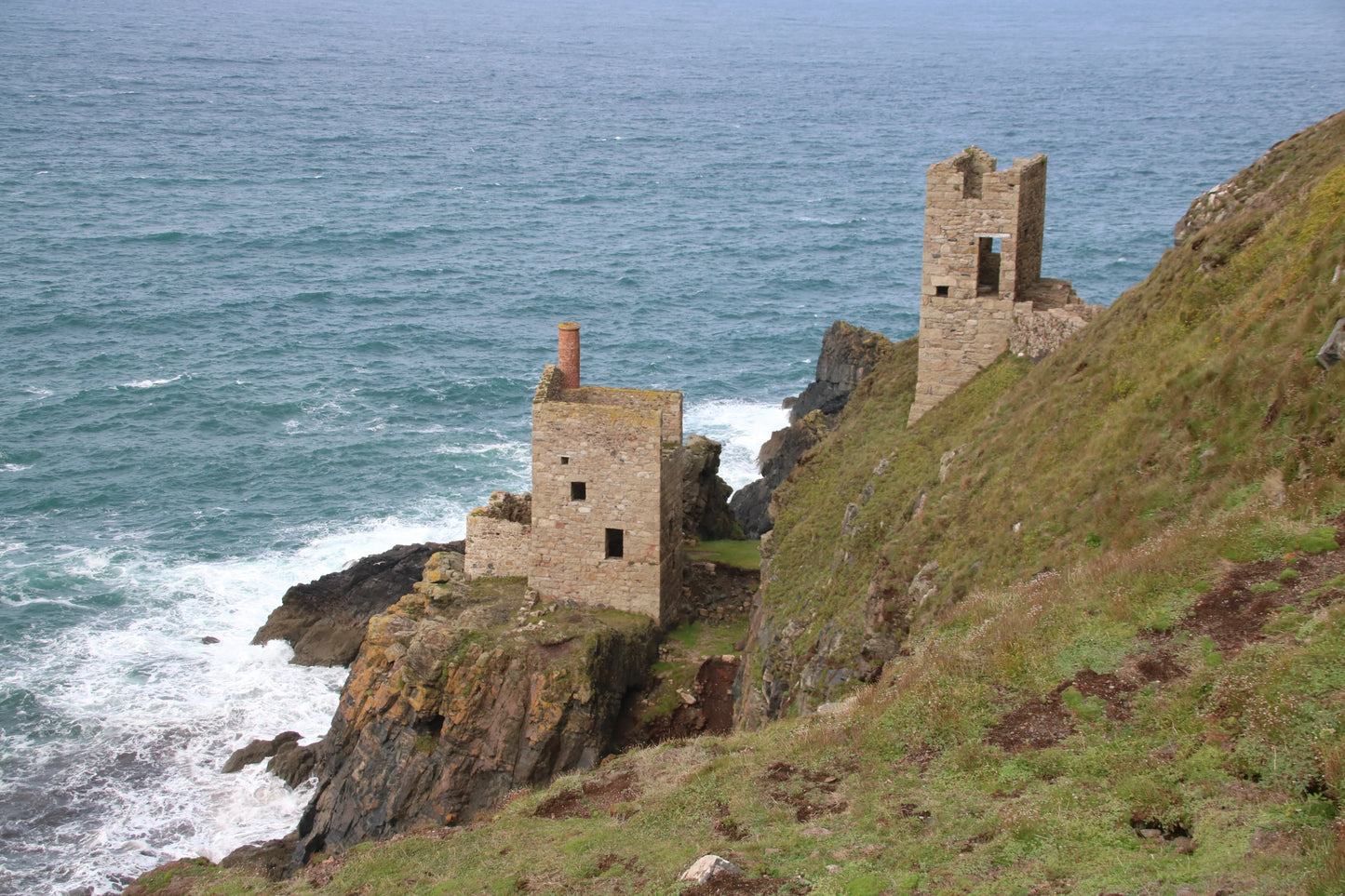 Ruins of historic stone mining buildings on rugged coastal cliffs above crashing sea waves