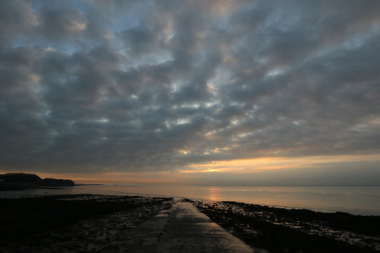 Sunset over calm sea with cloudy sky and rocky shoreline in British coastal landscape