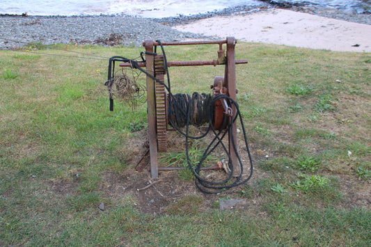 Rusty hand winch with coiled ropes on green grass by rocky shoreline