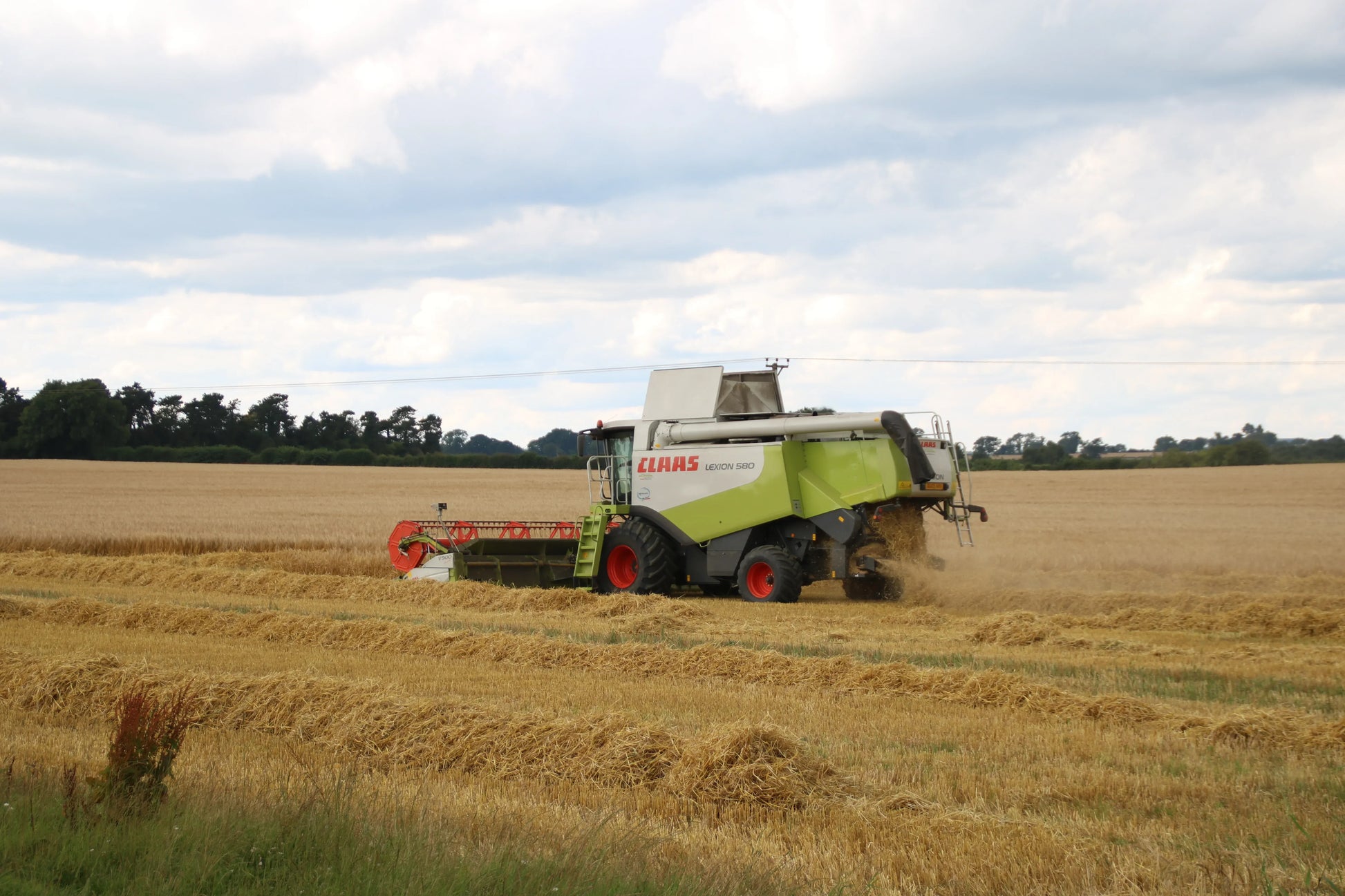 Claas Lexion 580 combine harvester working in a golden wheat field under a cloudy sky