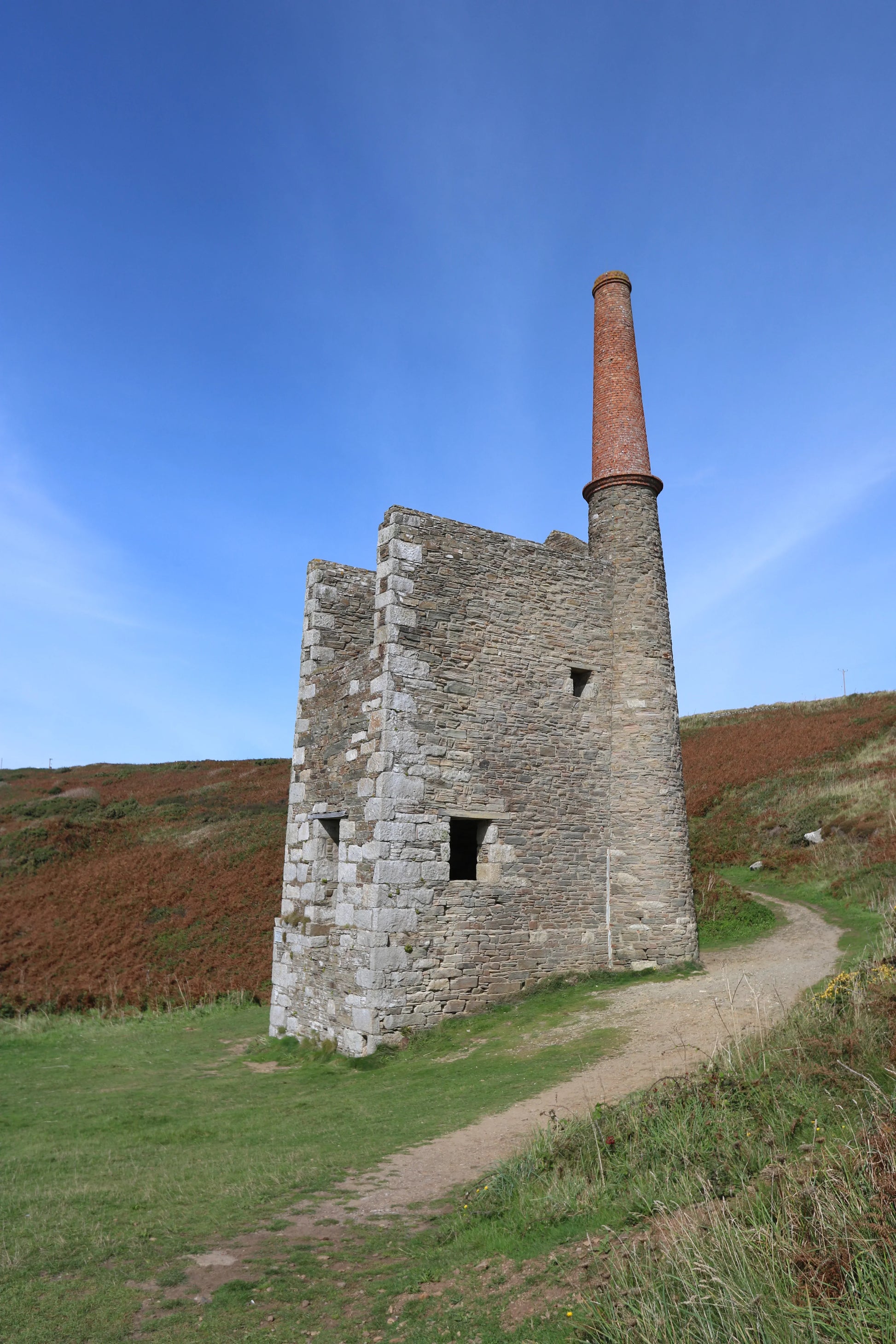 Historic Wheal Prosper tin mine engine house with tall brick chimney on moorland path at Rinsey Head Cornwall
