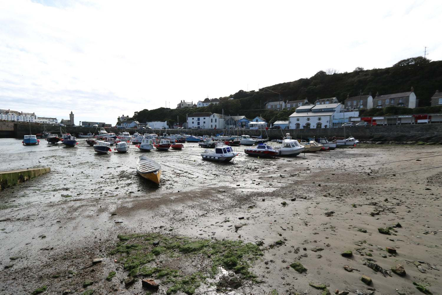 Low tide harbor with various small boats resting on muddy sand near coastal village houses