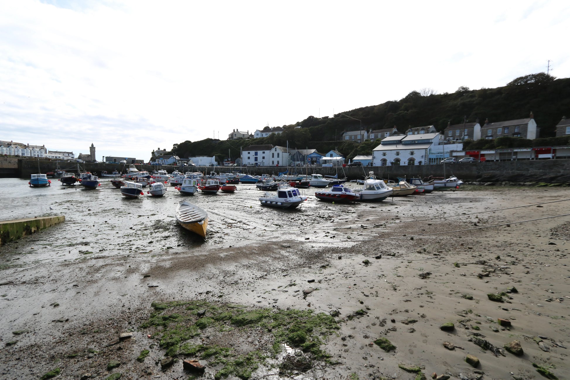 Low tide harbor with various small boats resting on muddy sand near coastal village houses