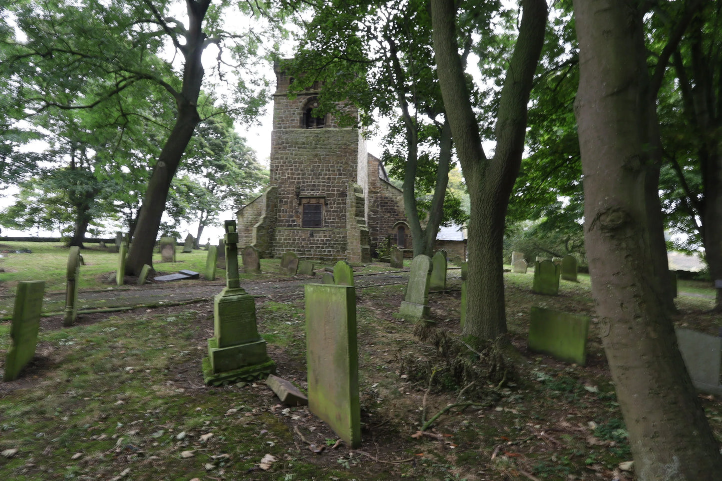 Historic stone church surrounded by moss-covered gravestones and mature trees in a shaded cemetery