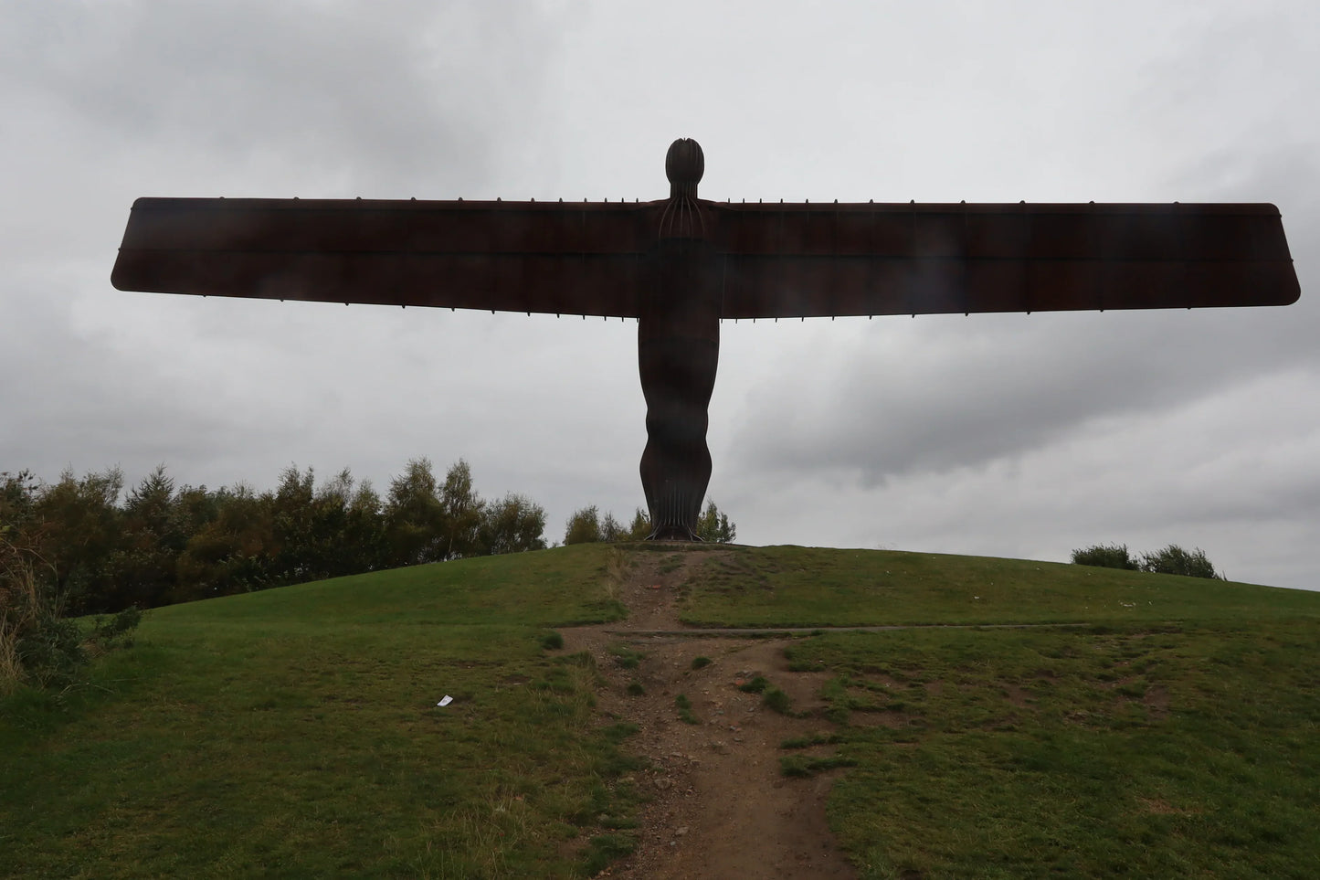 Silhouette of the Angel of the North sculpture on a grassy hill under cloudy sky