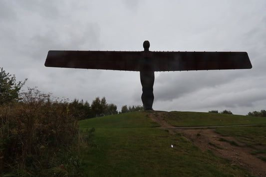 Silhouette of the Angel of the North statue on a grassy hill under cloudy sky