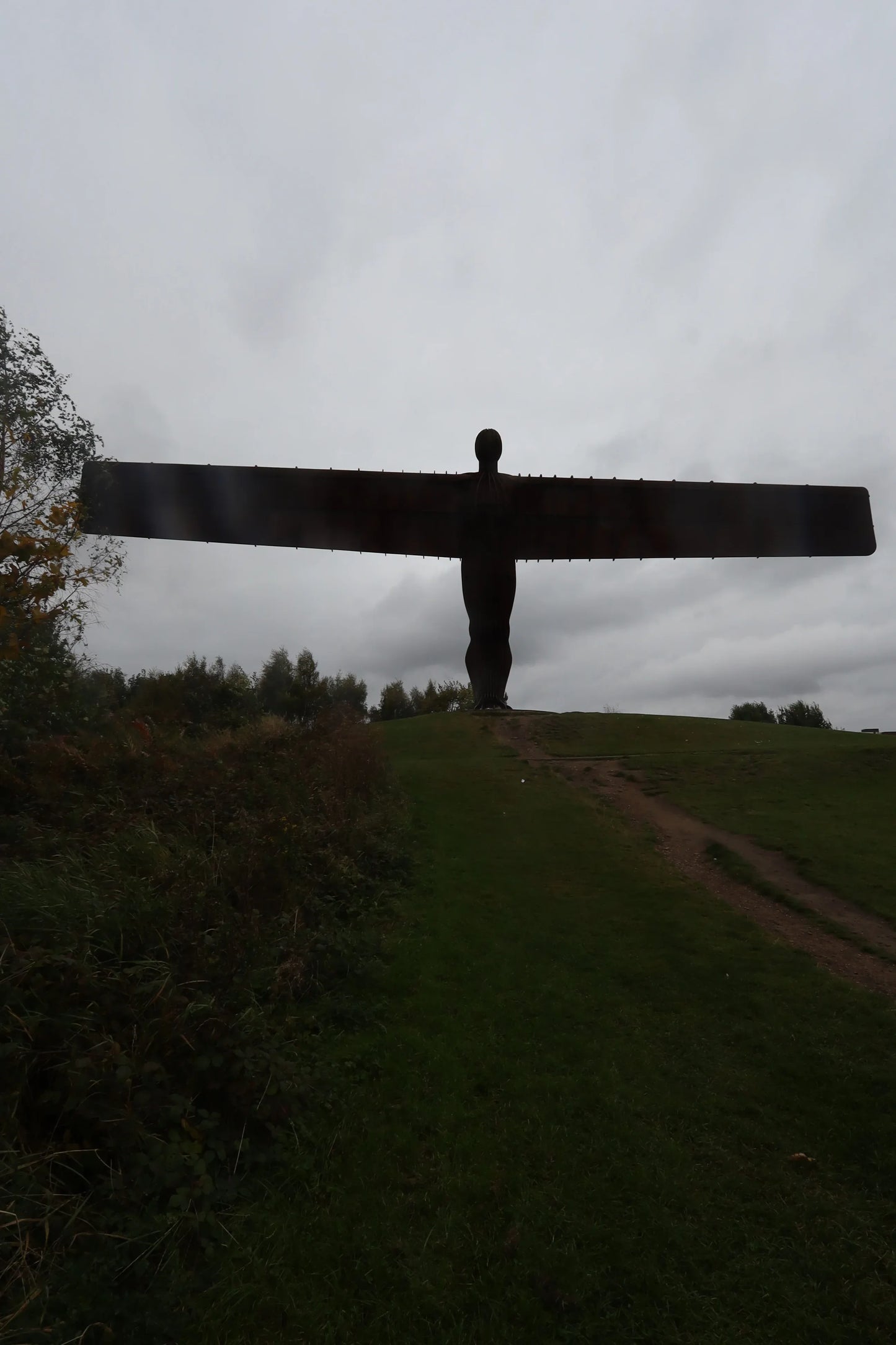 Silhouette of the Angel of the North sculpture on a grassy hill against a grey cloudy sky