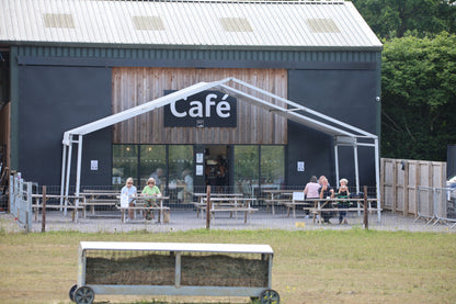Outdoor café seating with wooden picnic tables and customers in front of a modern barn-style building