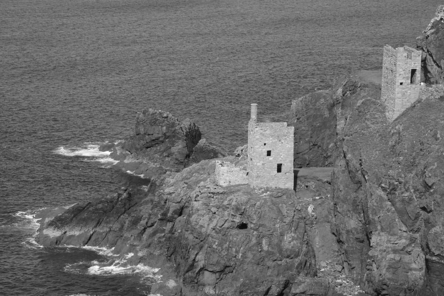 Black and white photo of old stone tin mine ruins on rocky coastal cliffs by the sea