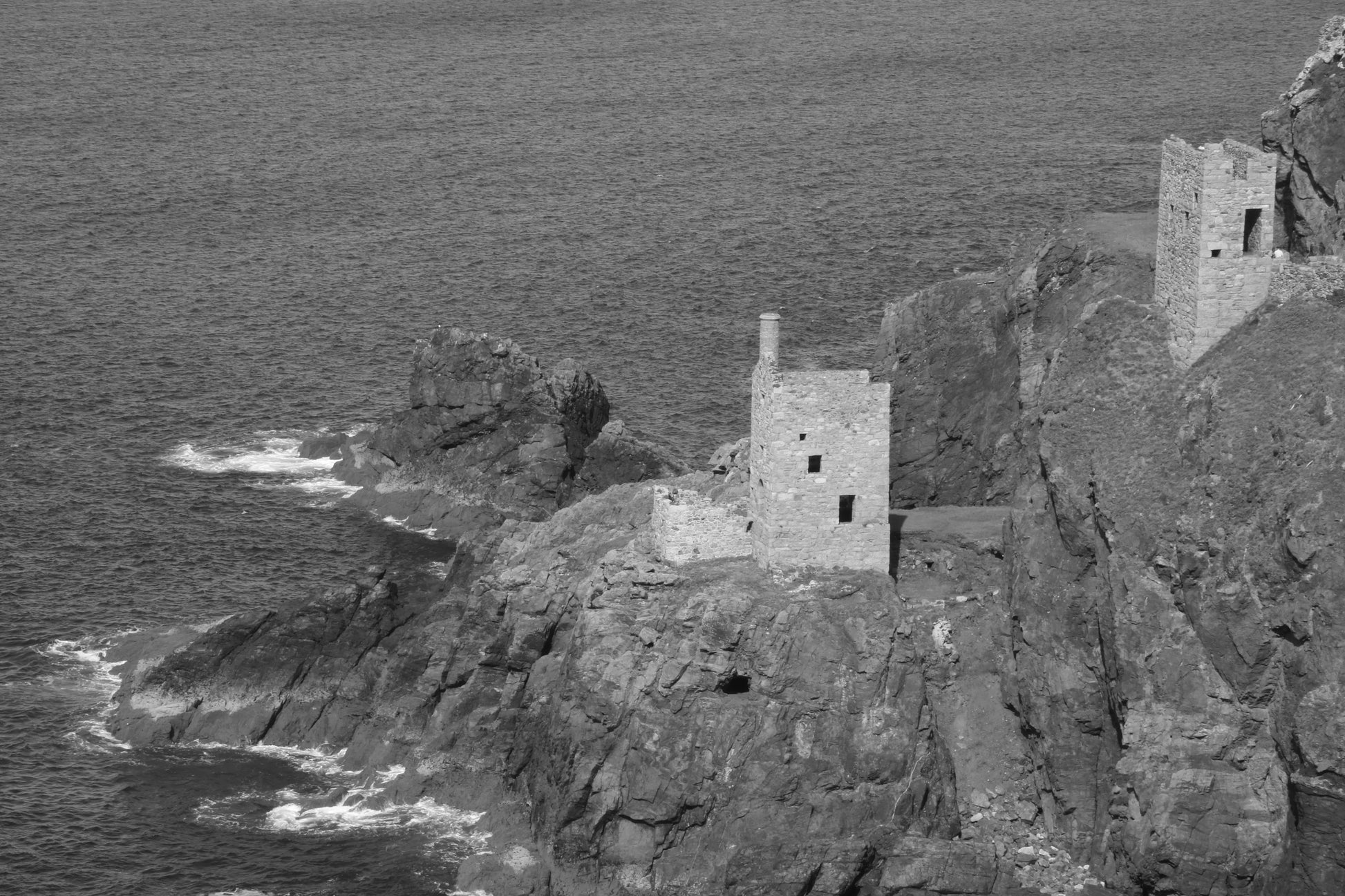 Black and white photo of old stone tin mine ruins on rocky coastal cliffs by the sea