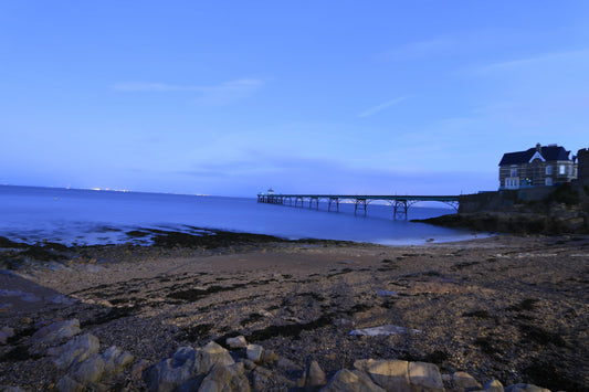 Clevedon Pier extending over calm sea at twilight with pebble beach and coastal house