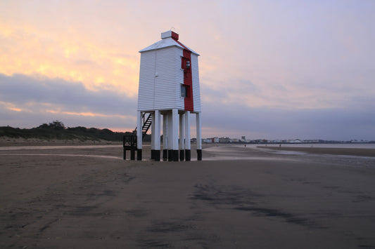 Burham-on-Sea wooden lighthouse on stilts at sunrise with sandy beach and distant town
