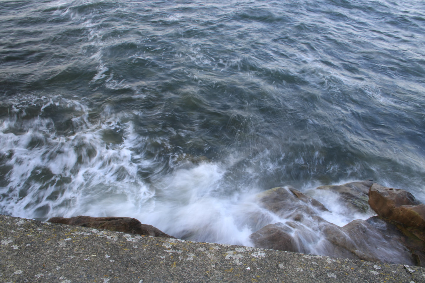 Waves crashing against rocky shore with textured concrete foreground, British coastal seascape