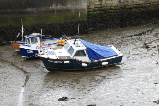 Two small boats stranded on muddy harbor bottom at low tide near mossy stone sea wall