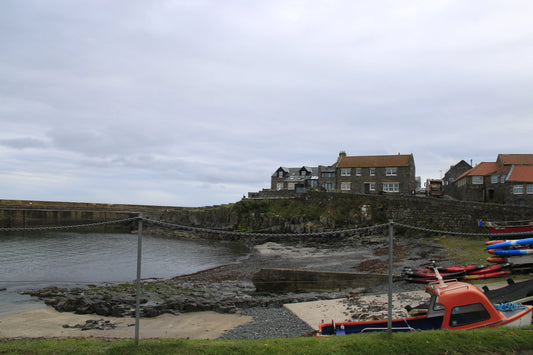 Coastal village harbor with stone houses, rocky shore, moored boat, and cloudy sky