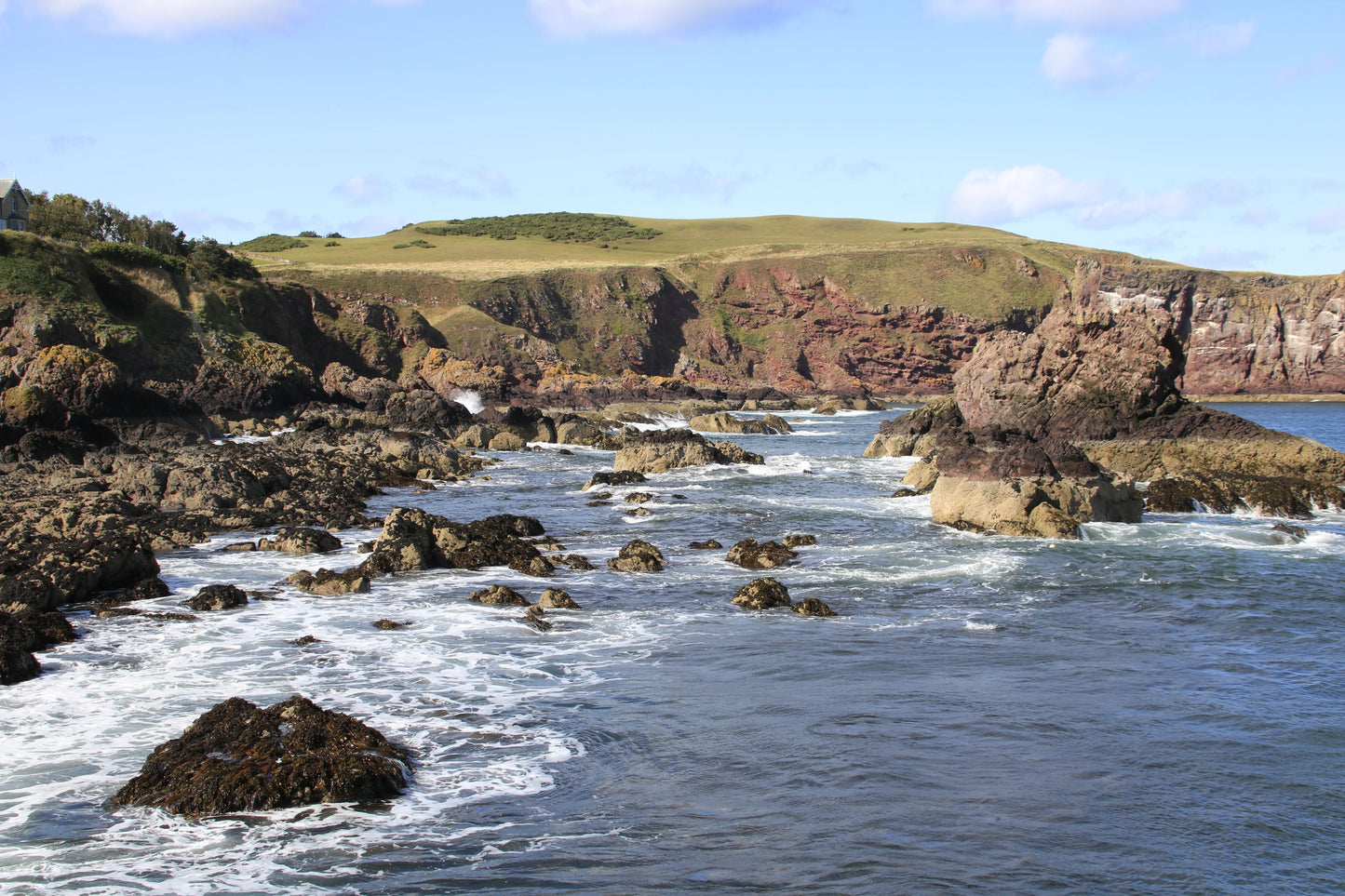 Rocky British coastline with waves washing over stones and grassy cliffs under blue sky