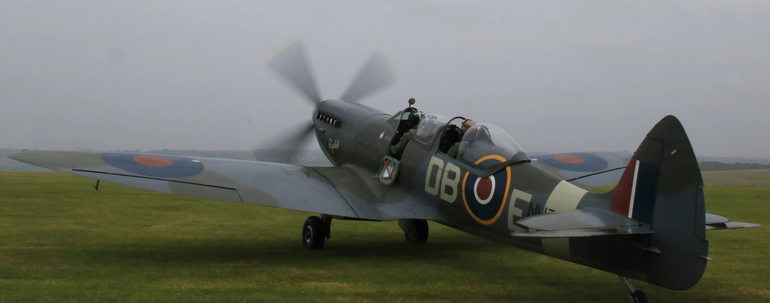 British Spitfire fighter aircraft on grass airfield with spinning propeller under cloudy sky