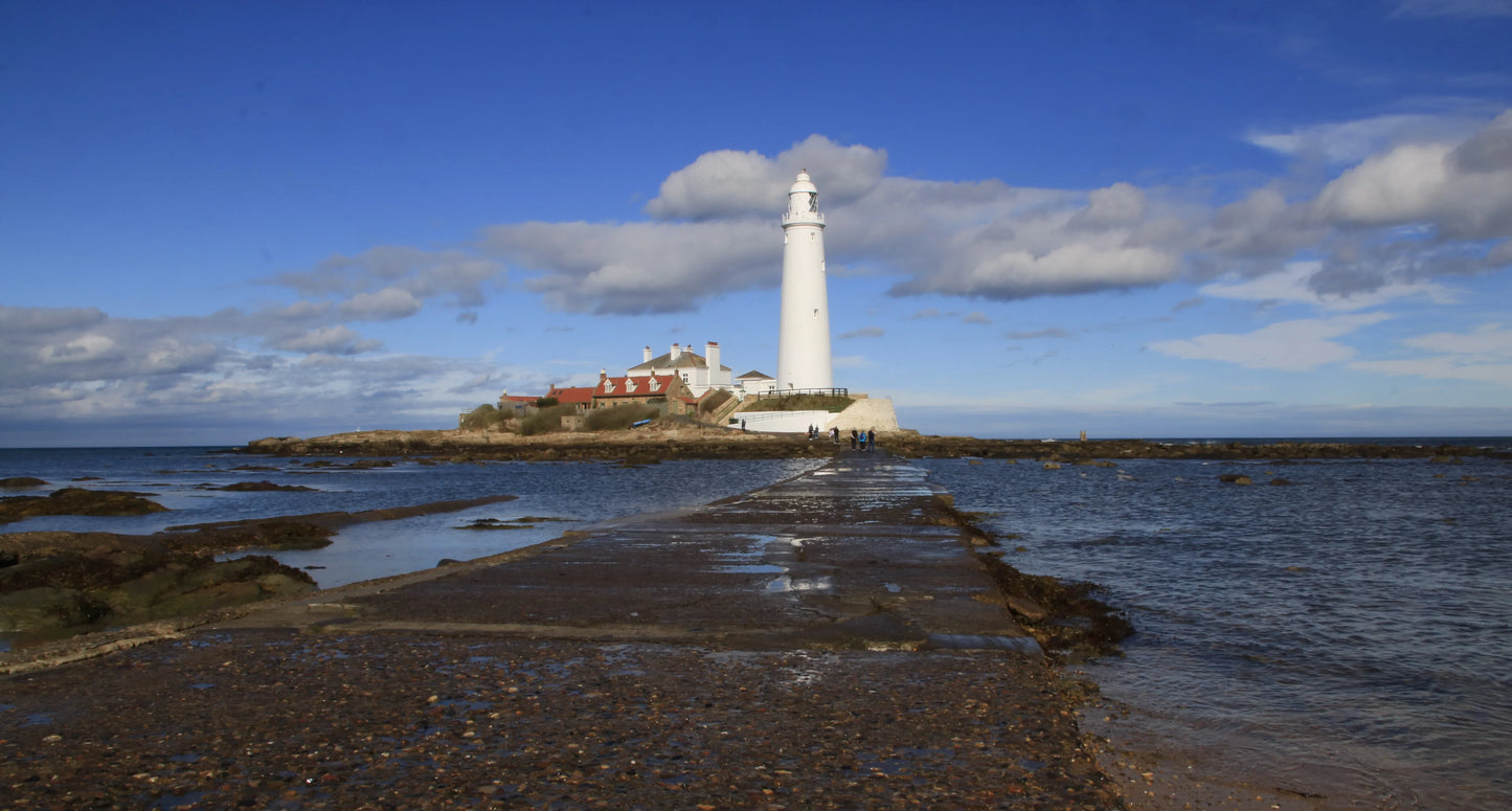 St Mary lighthouse on a rocky island connected by a causeway under blue sky, Northumberland coast landscape