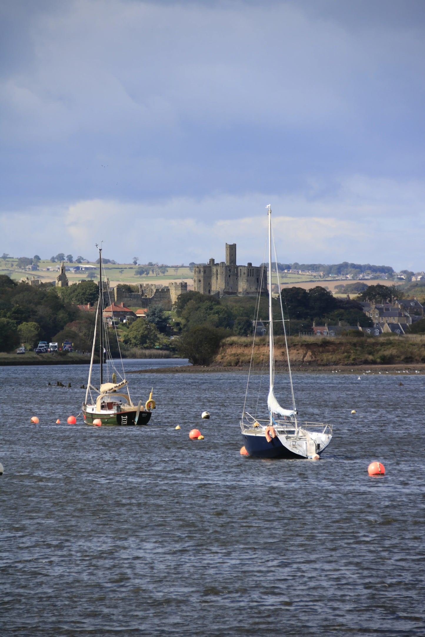 Northumberland coastal landscape with Warkworth Castle, moored sailboats, and buoys in calm water